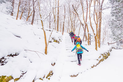 Full length of people hiking amidst bare trees on snow covered landscape