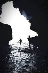 Silhouette people standing on rock by sea against sky