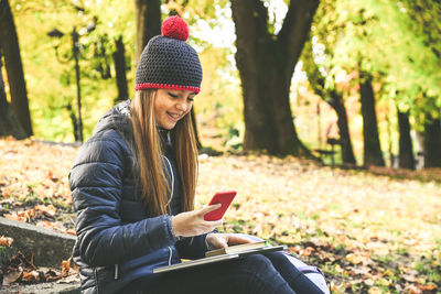 Girl with wool cap sitting in the park using smartphone. teen using mobile phone, chat with friends