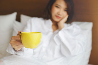 Close-up of woman holding coffee cup on bed at home