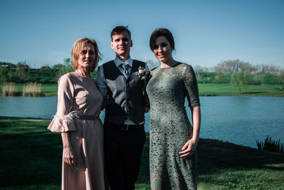 Young couple standing by lake against sky