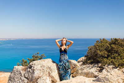 Man standing on rock by sea against clear sky