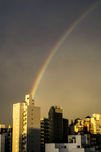 Low angle view of rainbow over buildings against sky