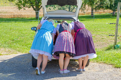 Women in dirndl bending by car on road
