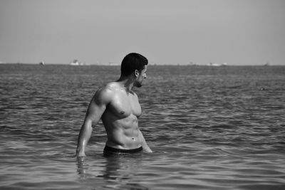 Full length of shirtless boy in sea against sky