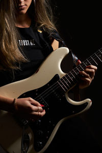 Midsection of woman playing guitar against black background