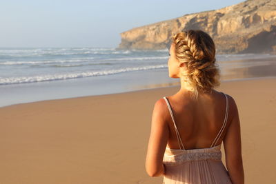 Rear view of woman standing at beach against sky