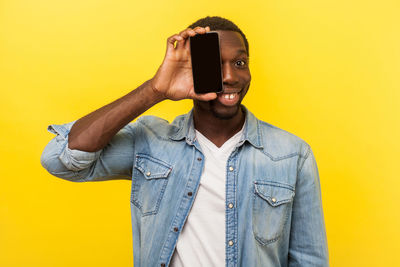Portrait of young man standing against yellow background