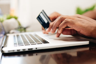 African american man at home using laptop computer to shop online with credit card in hand