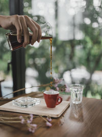 Midsection of person pouring drink in glass on table