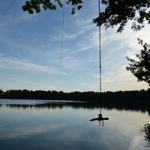 Silhouette person sitting on lake against sky during sunset