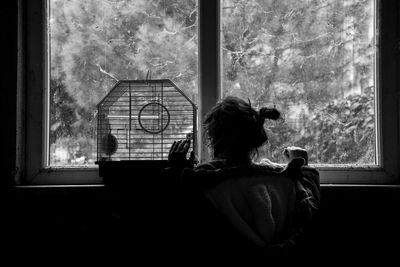 Rear view of woman looking through window at home