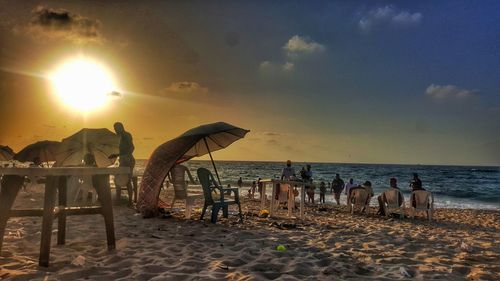 People at beach against sky during sunset