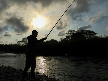 Silhouette man fishing on lake against sky during sunset