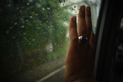 Close-up of hand on wet glass window in rainy season