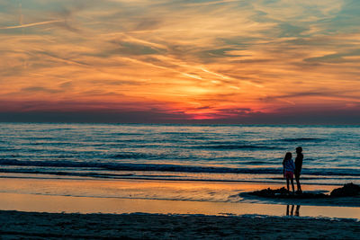 Silhouette people standing on beach against sky during sunset