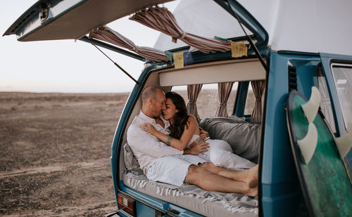 Gentle couple of travelers relaxing in van and tenderly hugging while enjoying vacation in savanna in summer