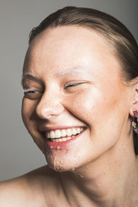 Close-up portrait of smiling young woman against gray background