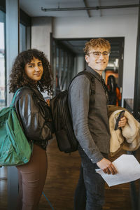 Smiling young male and female students looking back over shoulders in community college