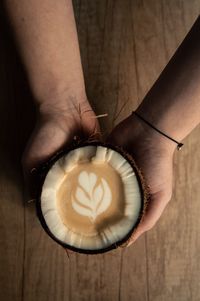 Cropped hands of young woman holding coffee in coconut on wooden table