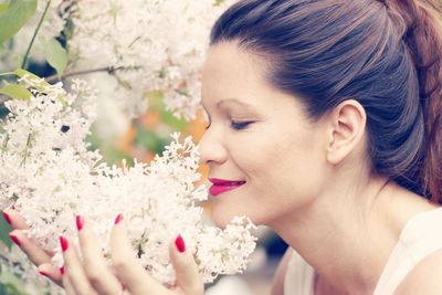 Close-up of smiling woman smelling white flowers growing on plants