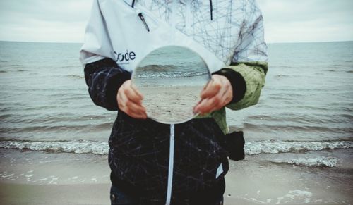 Man holding sunglasses while standing on beach