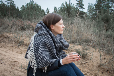 Side view of mature woman holding cup while sitting on field