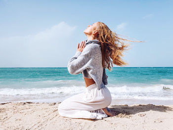 Side view of woman meditating on beach against sky