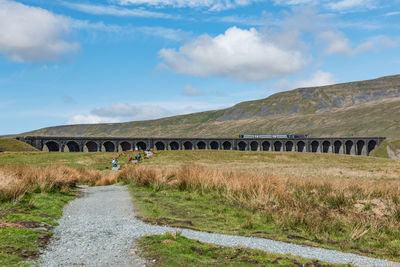 A train crossing ribblehead viaduct while hikers doing yorkshire three peaks challenge