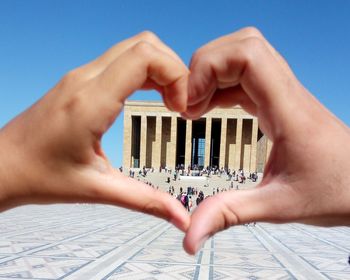 Building seen through heart shape made with hands