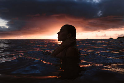 Woman standing by sea against sky during sunset