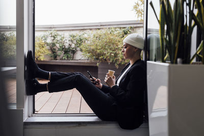 Young entrepreneur with coffee cup using mobile phone in office