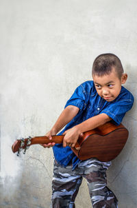 Boy playing with guitar while standing by wall