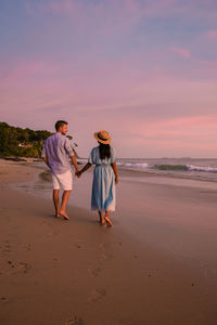 Rear view of couple holding hands walking on beach