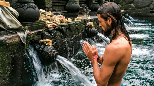 Midsection of shirtless man splashing water in temple