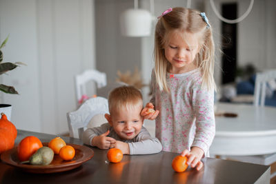 Siblings having oranges on table at home