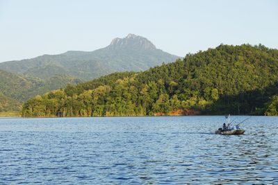 Mid adult man sitting in boat on lake against mountains