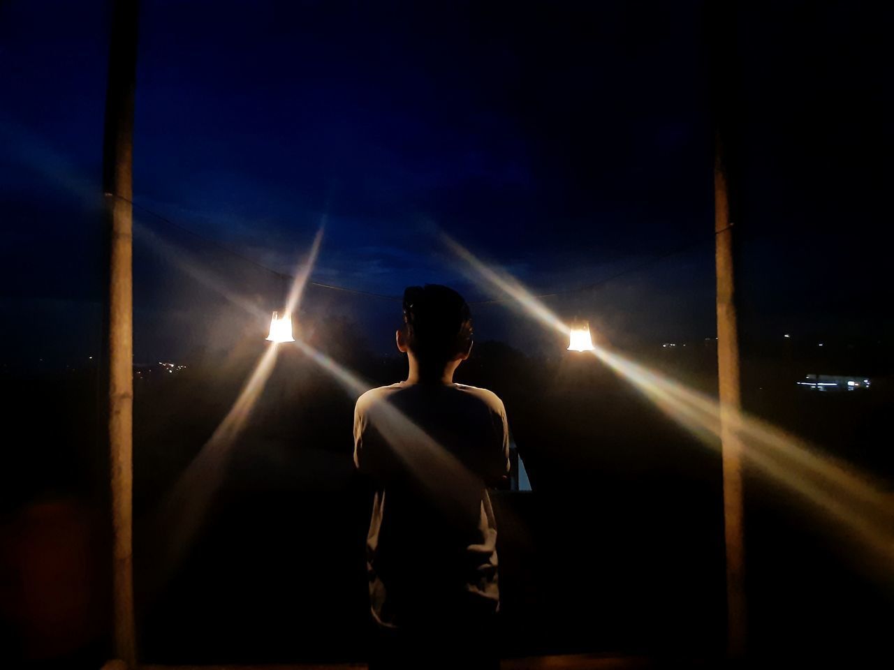 REAR VIEW OF WOMAN STANDING AGAINST ILLUMINATED SKY