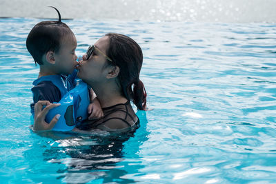 Mother kissing cute son in swimming pool