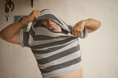 Man removing t-shirt while standing against wall at home