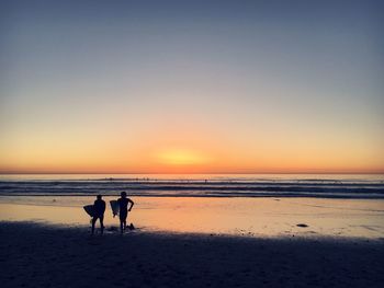 Silhouette dog on beach against sky during sunset