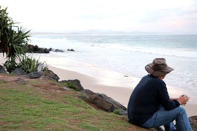 People sitting on beach looking at sea against sky