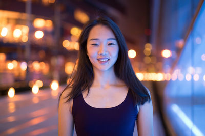 Portrait of smiling woman standing against illuminated lights at night