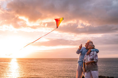 Man holding woman with umbrella against sky during sunset