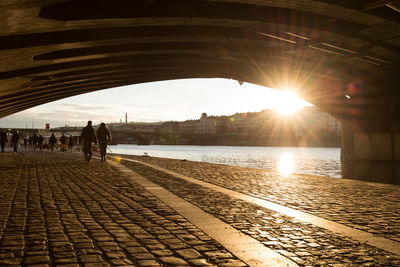 Bridge against people walking on footpath by vltava river at sunset