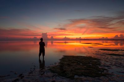 Silhouette man standing at beach against sky during sunset