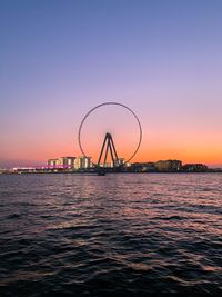 Ferris wheel by sea against clear sky during sunset