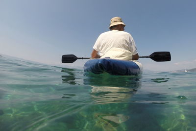 Rear view of man kayaking in sea against sky