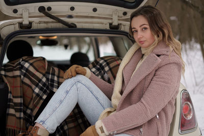 Young woman sitting in car trunk