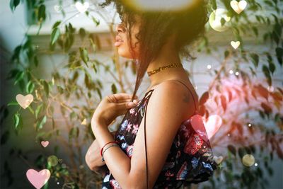 Side view of woman holding hair while standing by plants